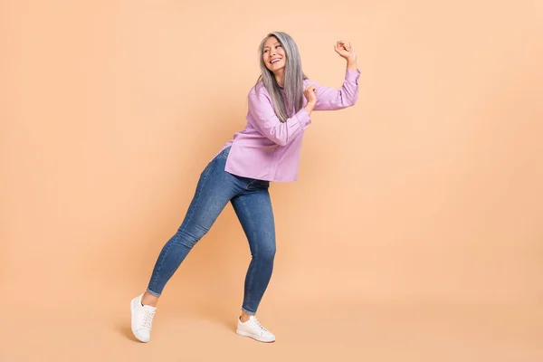 Фотографія повного розміру прохолодного білого зачіски у віці леді-танцюють просування одягу фіолетові сорочки джинси кросівки ізольовані на бежевому фоні — стокове фото