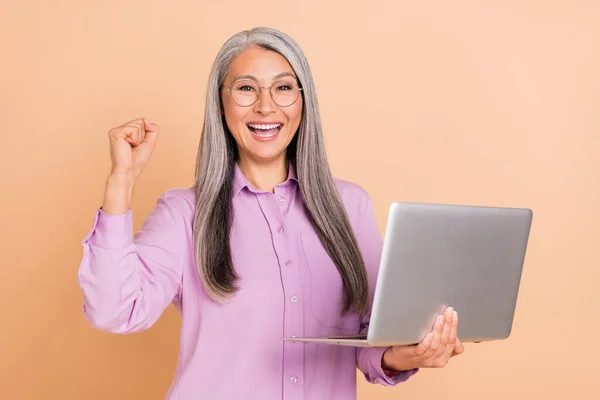 Zdjęcie funky białe włosy starsza pani trzymać laptop krzyczeć nosić okulary fioletowy koszula izolowane na beżowym tle — Zdjęcie stockowe