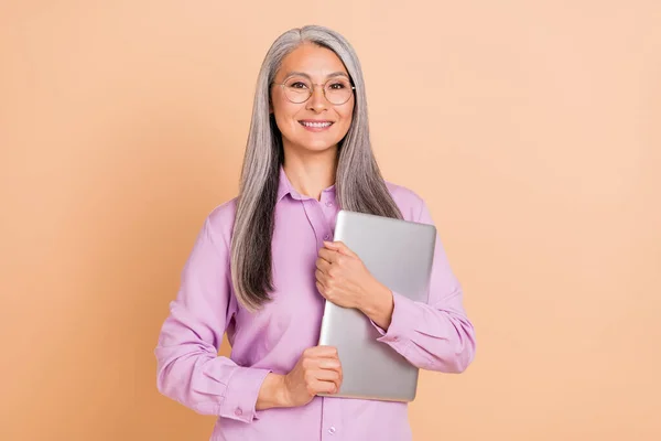 Foto de jefe peinado blanco señora anciana celebrar portátil usar gafas camisa violeta aislado sobre fondo beige —  Fotos de Stock