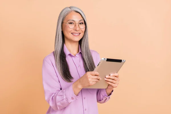Foto di ottimistico bianco acconciatura sambuco signora scrivere tablet indossare occhiali camicia viola isolato su sfondo di colore beige — Foto Stock