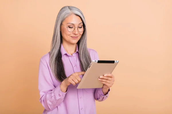 Foto do penteado cinza inteligente idade senhora tipo tablet desgaste óculos camisa violeta isolado no fundo cor bege — Fotografia de Stock