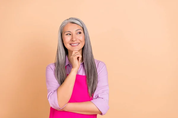 Photo of funny white hairdo aged lady look empty space wear purple shirt pink apron isolated on beige color background — Stock Photo, Image