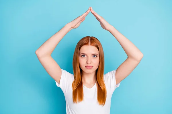 Foto de braços de menina de cabelo laranja bastante satisfeito fazer figura da casa acima da cabeça isolada no fundo de cor azul — Fotografia de Stock