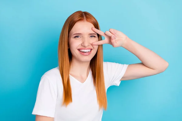 Foto de bastante positivo laranja cabelo pessoa irradiando sorrir dedos mostrar v-sinal perto do olho isolado no fundo de cor azul — Fotografia de Stock