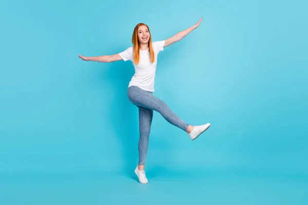 긍정적 인 미소를 짓고 있는 어린 소녀의 전신 사진은 파란 색 배경 위에 격리 된 재미있는 손 날개 비행기를 갖고 있다 — 스톡 사진