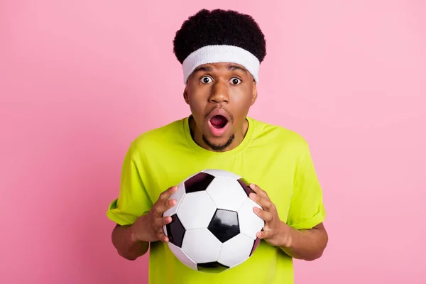 Фото изумленного шокированного афро-американского юноши, держащегося за руки футбола, изолированного на розовом фоне — стоковое фото