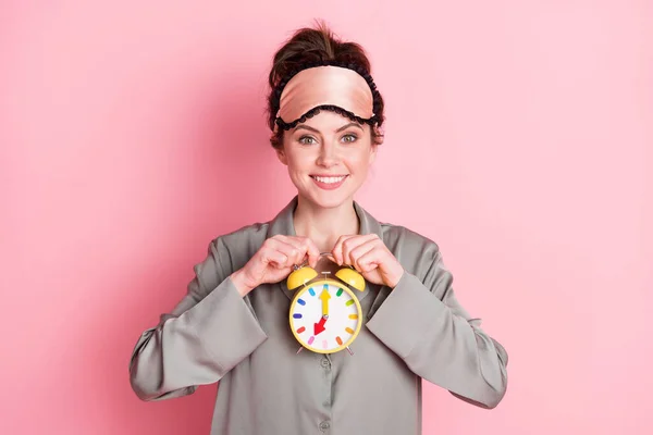 Retrato de menina alegre atraente usando pijama segurando em mãos relógio infantil isolado sobre fundo cor pastel rosa — Fotografia de Stock