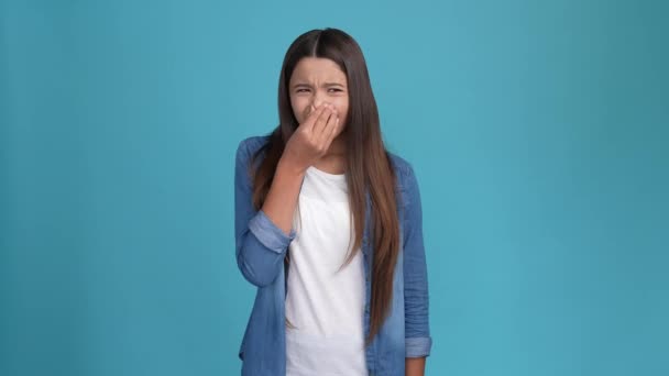 Niña cubierta dedos nariz evitar olor aislado color azul fondo — Vídeos de Stock