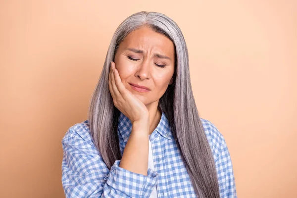 Фото хворої леді пенсіонерки, одягнена в картату сорочку рука щоки зуби біль ізольований бежевий кольоровий фон — стокове фото
