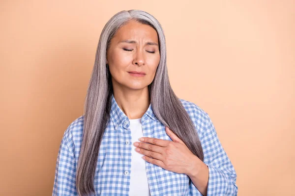 Фото нещасливої засмученої жінки, яка носить плетену сорочку рука грудей закритих очей серцевий напад ізольований бежевий кольоровий фон — стокове фото