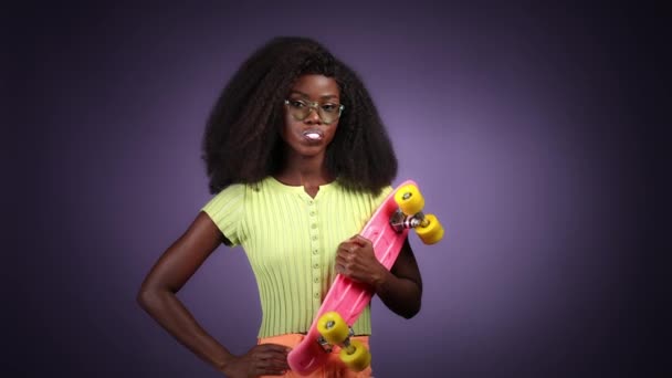 Lady verspielt halten Skateboard blasen Blasenkaugummi isoliert dunkle Farbe Hintergrund — Stockvideo
