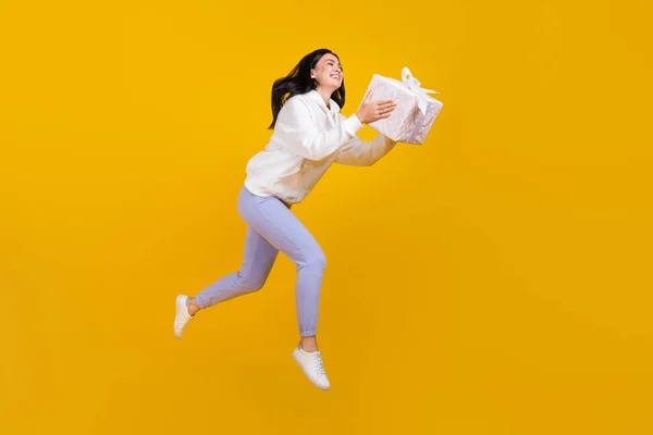 Φωτογραφία προφίλ του αρκετά χαρούμενη κυρία άλμα κρατήσει το παρόν κουτί φορούν λευκό hoodie απομονωμένο κίτρινο χρώμα φόντο — Φωτογραφία Αρχείου