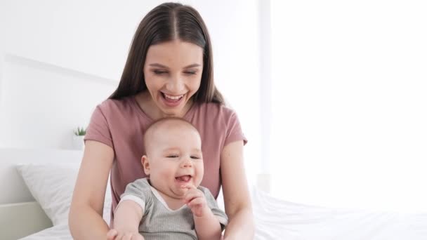 Adorável terapeuta menina massagem bebê menino pernas jogando cama dentro de casa — Vídeo de Stock