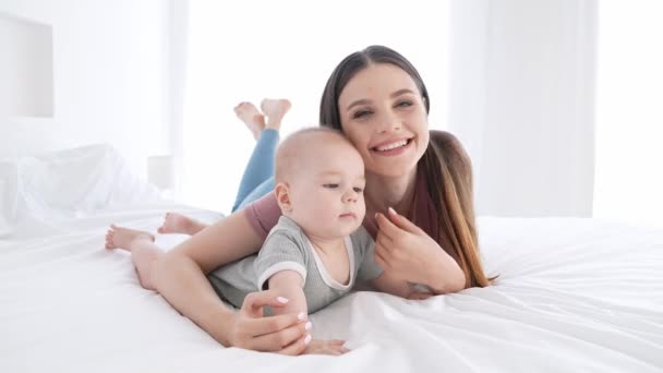 Lindo dulce mami acostado cama abrazo bebé niño cuidado de niños en el interior — Vídeos de Stock
