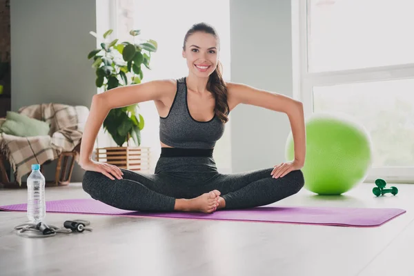 Foto de sexy mujer joven flexible usar traje deportivo sonriente estiramiento piernas practicando yoga en interiores casa —  Fotos de Stock