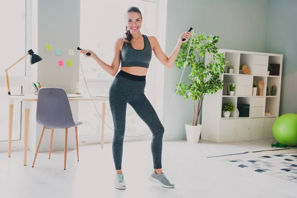 Foto de divertida chica sexy vestido traje deportivo saltar la cuerda sonriendo en el interior de la casa de casa —  Fotos de Stock