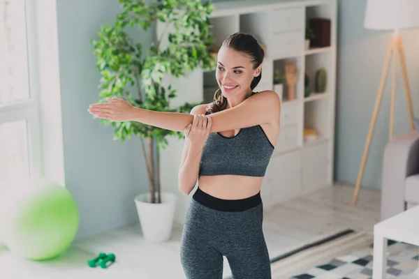 Foto av drömmande förtjusande dam bära sport outfit leende stretching hand arm inomhus hus — Stockfoto