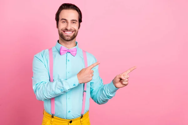 Foto de hombre joven divertido impresionado usar traje de turquesa sonriendo señalando dos dedos espacio vacío aislado color rosa fondo — Foto de Stock