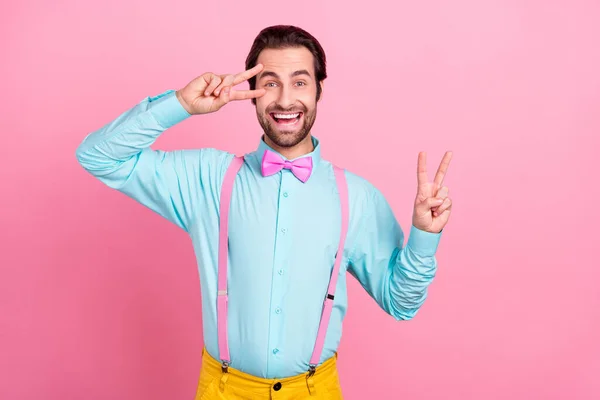 Foto av opphisset, barnslig, ung mann kledd i turkis som viser to V-tegn på øyesyn smilende, isolert, rosa bakgrunn – stockfoto