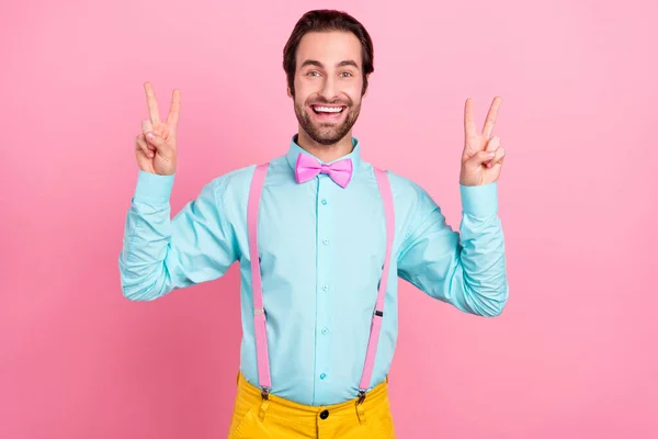 Foto de un joven bastante impresionado usar traje de color turquesa sonriendo mostrando dos signos de v aislado de color rosa de fondo — Foto de Stock