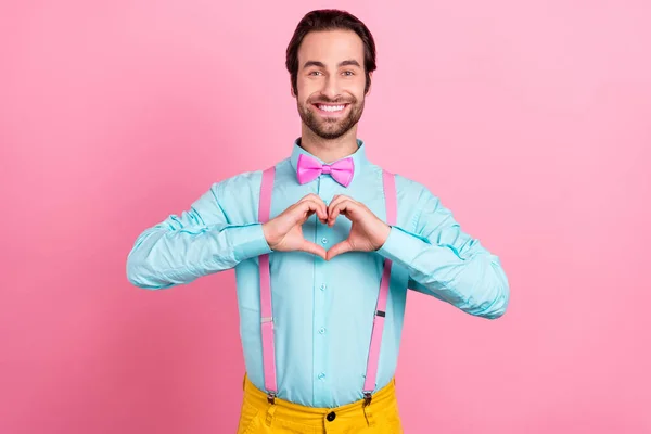Φωτογραφία από γοητευτικό όμορφο νεαρό άνδρα φορούν τιρκουάζ στολή χαμογελώντας δείχνοντας τα χέρια καρδιά απομονώνονται ροζ χρώμα φόντο — Φωτογραφία Αρχείου
