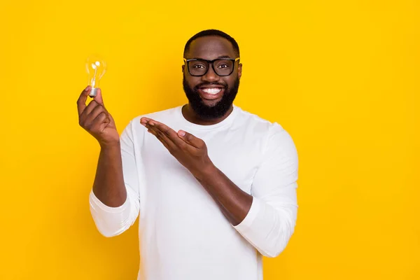 Портрет откровенного веселого человека рука держать шоу лампочка сияющая улыбка изолированы на желтом фоне цвета — стоковое фото