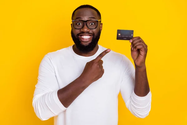 Fotografie pozitivního veselý chlap indikovat prst debetní plastové karty propagace izolované na žlutém pozadí — Stock fotografie