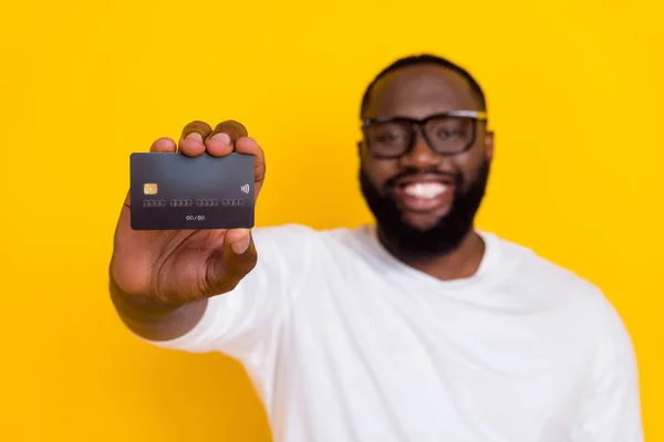 Foto de cara positivo desfocado braço segurar cartão de débito de plástico irradiando sorriso isolado no fundo de cor amarela — Fotografia de Stock