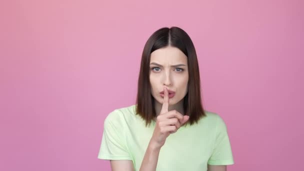 ผู้หญิงที่เข้มงวดขอไม่พูดปากซุบซิบนิ้วแยกพื้นหลังสีชมพู — วีดีโอสต็อก