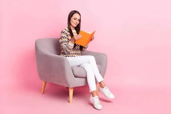 Фото мрійливої блискучої молодої жінки, одягненої в пунктирний светр, усміхнений сидячим кріслом, читає книгу про порожній простір ізольований рожевий колір фону — стокове фото