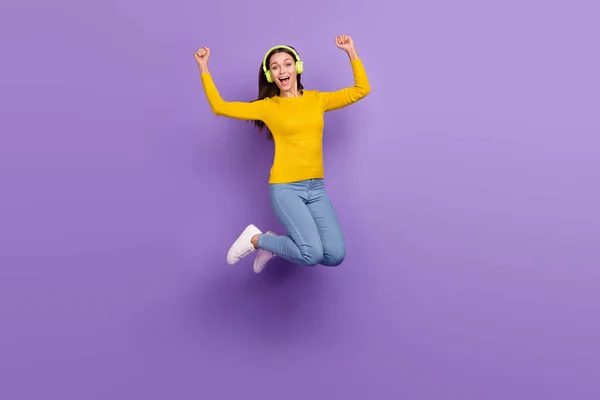 Foto de longitud completa de chica joven divertirse salto regocijarse victoria escuchar auriculares de radio aislados sobre fondo de color púrpura — Foto de Stock