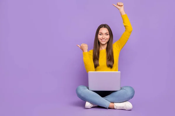 Full size photo of young lady sit floor hold laptop indicate fingers empty space ads promo isolated over violet color background — Stock Photo, Image
