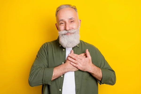 Foto porträtt av senior man ler tacksamt hålla händerna på bröstet isolerad levande gul färg bakgrund — Stockfoto