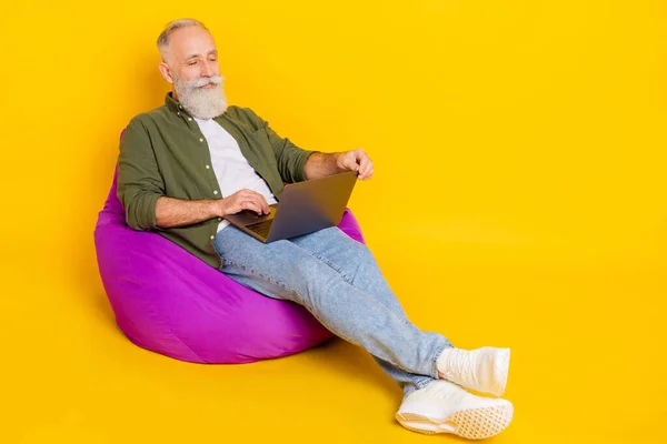 Photo de smart freelance vieil homme assis sac tenir netbook porter chemise verte isolé fond de couleur jaune — Photo
