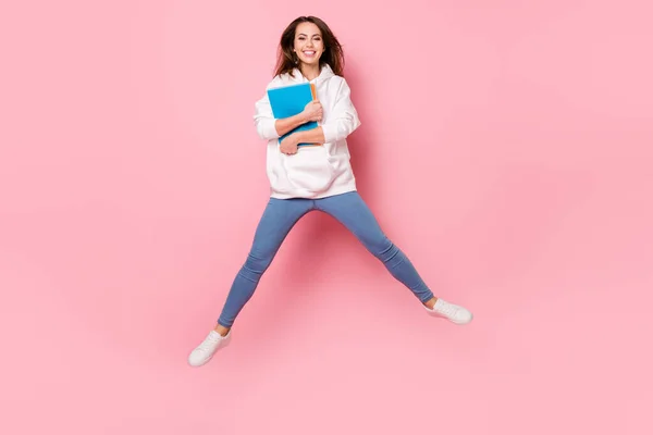 Foto de adorable bonita joven vestida con sudadera blanca sosteniendo copybooks saltando alto sonriente aislado color rosa fondo — Foto de Stock