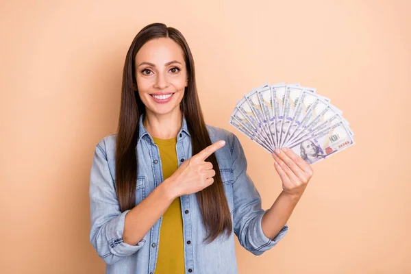 Ritratto di splendida ragazza positiva punta il dito soldi raccomandando pubblicizzare isolato su sfondo di colore beige — Foto Stock