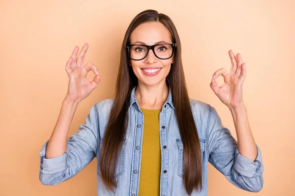 Foto av glada leende dam visar okej gest bära glasögon denim casual skjorta isolerad på beige färg bakgrund — Stockfoto