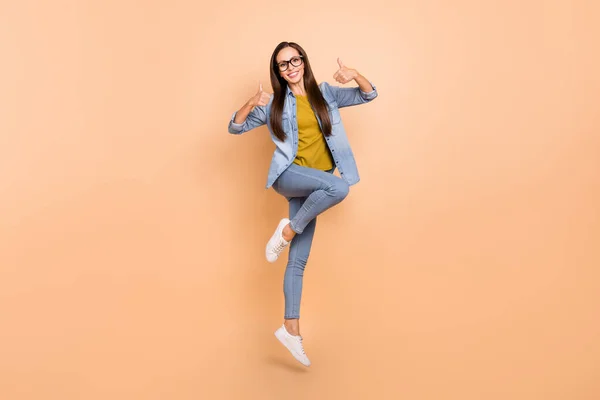 Foto de tamaño completo de salto bastante femenina muestran el pulgar hacia arriba recomendando usar ropa de mezclilla aislada sobre fondo de color beige — Foto de Stock