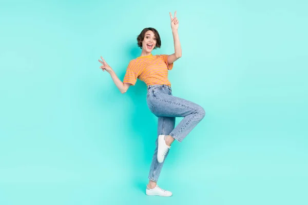 Foto de encantadora linda mujer joven vestida a rayas camiseta sonriente bailando mostrando signos de v aislado color verde azulado fondo — Foto de Stock