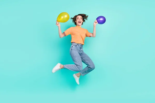 Фото солодкої збудженої молодої жінки, одягненої в смугасту футболку, усміхнені стрибки, що тримають повітряні кулі ізольованого кольорового фону — стокове фото