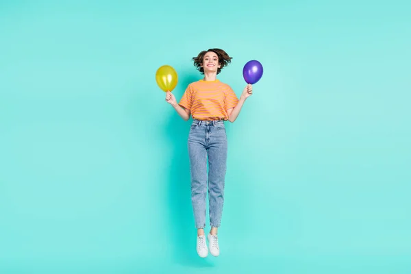Foto di eccitato affascinante giovane donna vestita a righe t-shirt sorridente salto tenendo due palloncini isolato colore verde acqua sfondo — Foto Stock