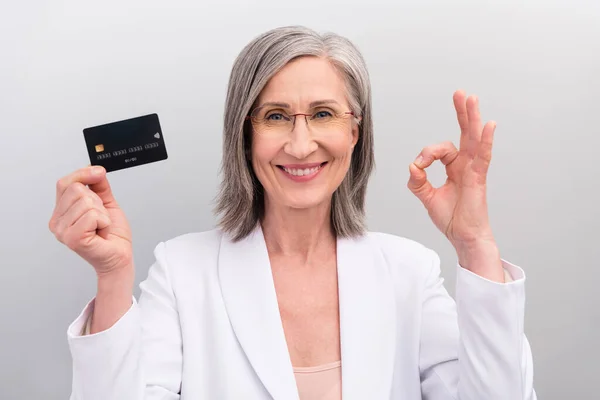 Foto de penteado branco engraçado envelhecido trabalho senhora mostrar cartão okey desgaste colete isolado no fundo de cor cinza — Fotografia de Stock