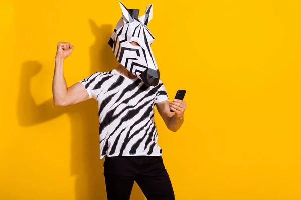Fotografie vzrušený blázen chlap blogger v zebra maska použít chytrý telefon pěst nahoru win followers post izolované přes žluté barvy pozadí — Stock fotografie