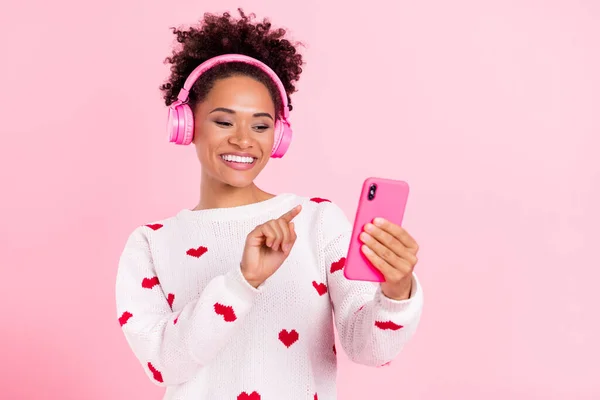 젊은 아프리카 소녀의 사진 스마트폰처럼 보이는 스마트 폰은 핑크 색 배경 위로 분리 된 노래 헤드폰을 선택 한다 — 스톡 사진