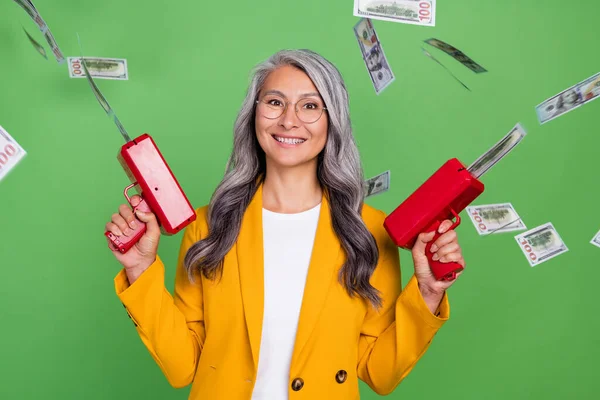 Foto di anziana bella donna sparare soldi milionario occhiali giocattolo isolato su sfondo di colore verde — Foto Stock