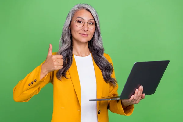 Foto de mulher sênior segurar laptop mostrar escolha thumb-up sugerir advogado anúncio isolado sobre fundo cor verde — Fotografia de Stock