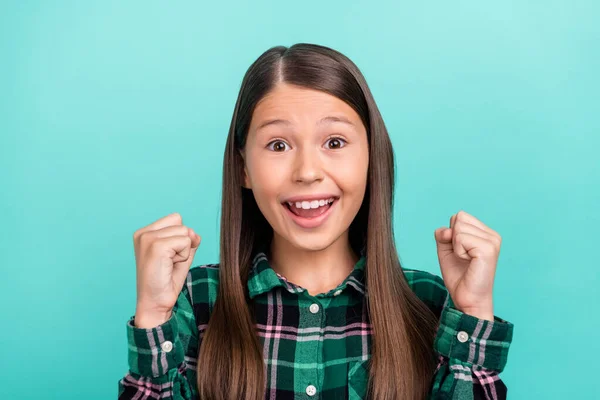 Foto de adorável menina da escola sorte vestida roupas xadrez sorrindo levantando punhos isolado cor teal fundo — Fotografia de Stock