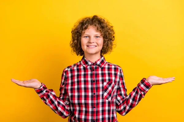 Photo de coiffure bouclée orange funky petit garçon tenir espace vide porter chemise à carreaux rouge isolé sur fond de couleur jaune — Photo