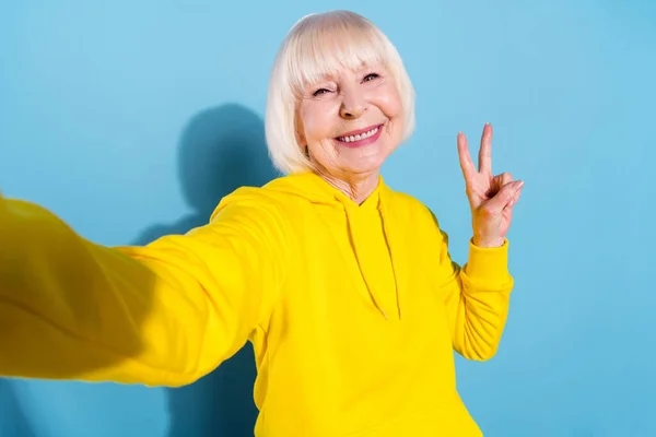 Fotografie pozitivní veselá stará žena, aby selfie show V-sign pozdrav cool izolované na modrém pozadí — Stock fotografie
