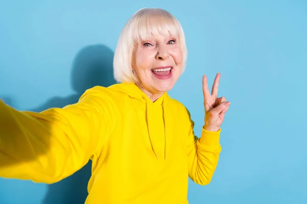 Fotografie veselá stará žena dobrá nálada vzít selfie, aby V-sign ahoj izolované na pastelové modré barvy pozadí — Stock fotografie